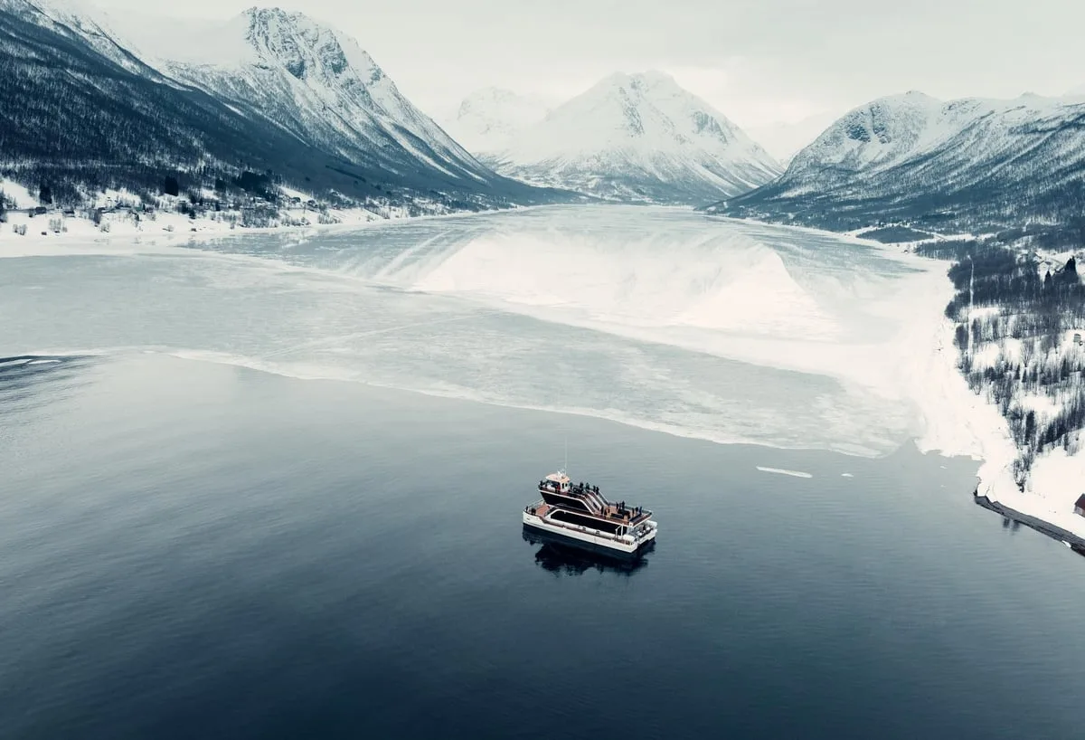 Cruise vessel on a calm fjord below snowy mountains